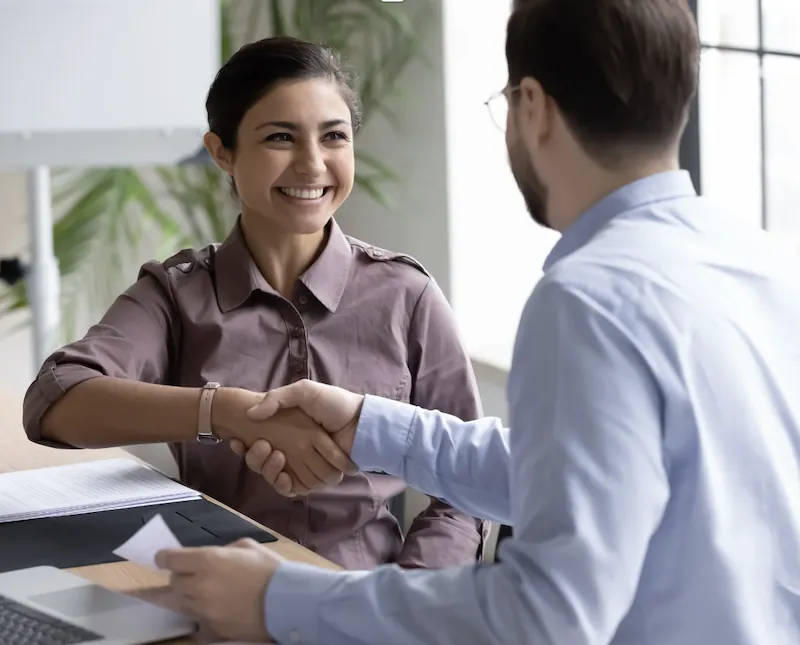 Une candidate souriante serre la main de son recruteur à la fin de l’entretien